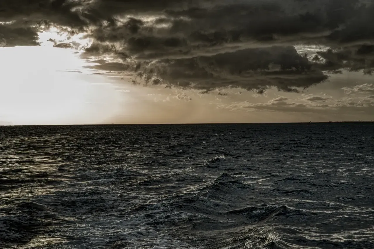 A dark sky over the ocean with waves in front of it.